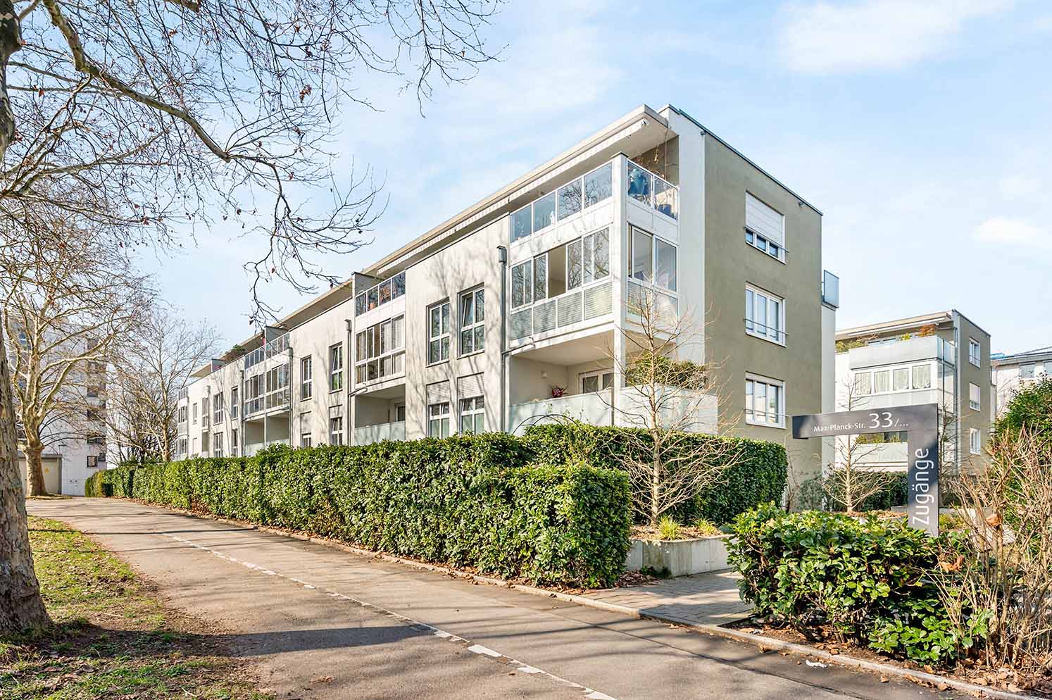 Mehrgeschossiger, moderner Wohnkomplex mit großen Balkonen und gepflegter Begrünung entlang eines Gehwegs.