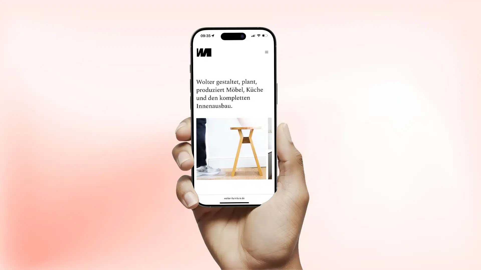 Hand hält ein Smartphone, auf dem die mobile Website von Wolter Furniture mit Text zu Möbel-, Küchen- und Innenausbauleistungen sowie einem Foto eines Holzhockers zu sehen ist.