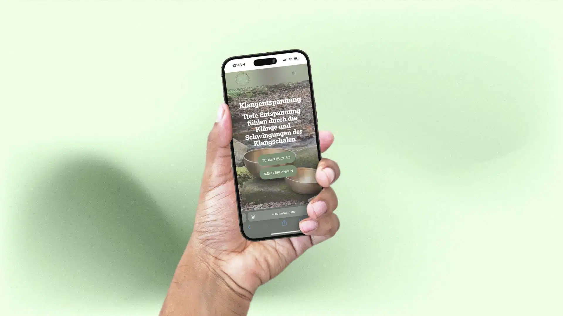 Hand hält ein Smartphone, auf dem die mobile Website von Tanja Kuhn mit der Überschrift Klangentspannung und den Buttons Termin buchen und Mehr erfahren zu sehen ist.
