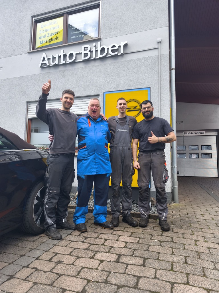 Vier Mitarbeiter von Auto Biber stehen vor dem Autohaus und geben vor dem Eingangsbereich ein positives Teamfoto ab.